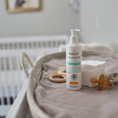 Noleo diaper care product on a textured surface with baby items in a nursery setting