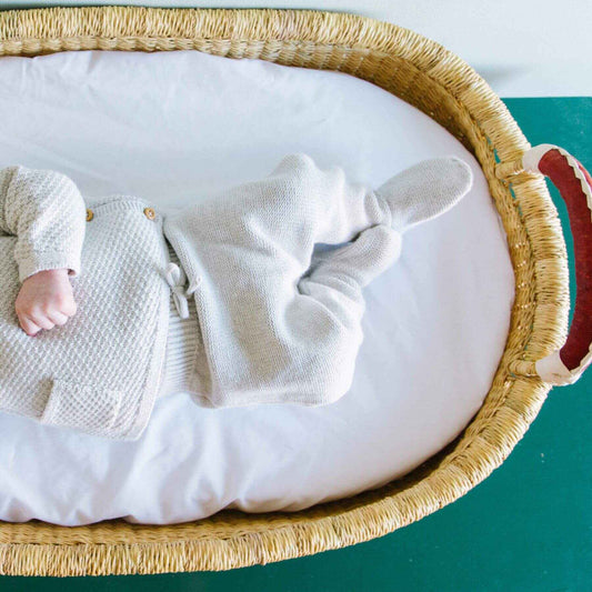 Baby in a textured outfit lying in Plum+Sparrow Changing Basket with a white mattress on a teal background