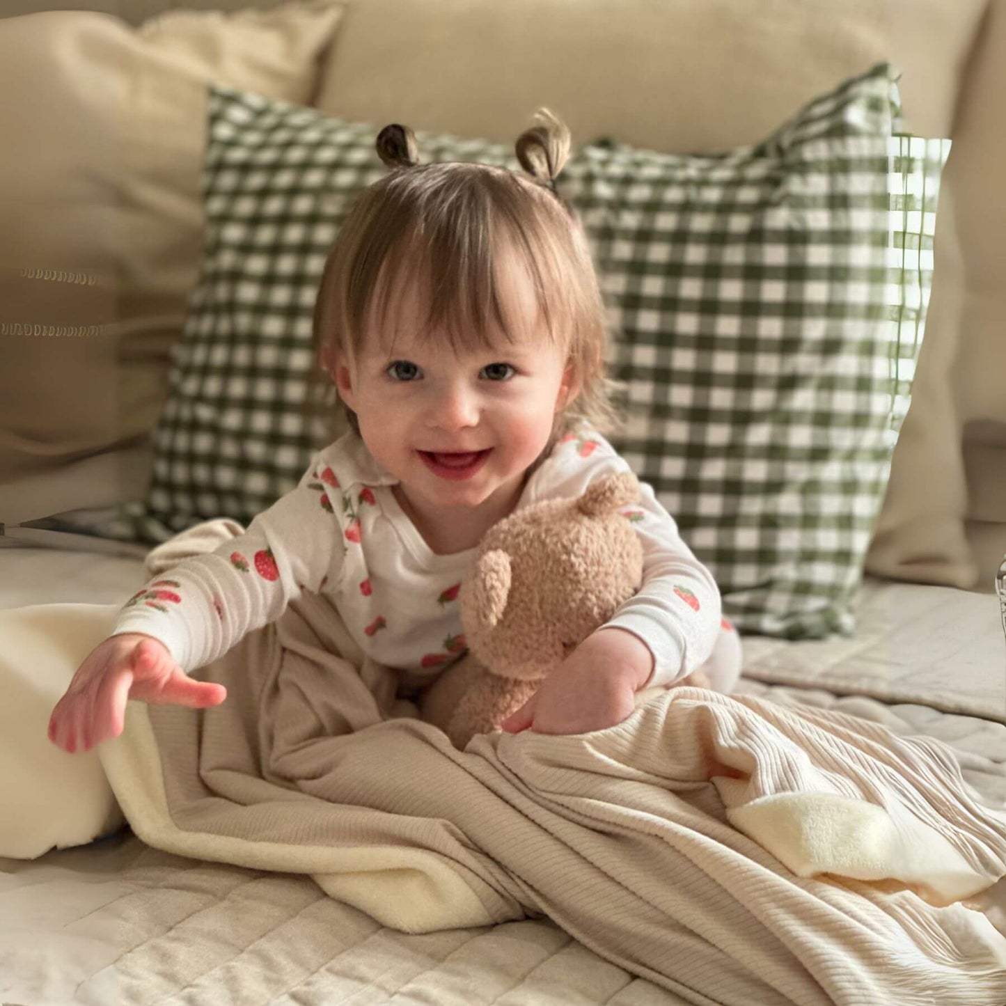 Child holding a teddy bear on bed with Little Mae & Co Oat Ribbed Toddler Blanket