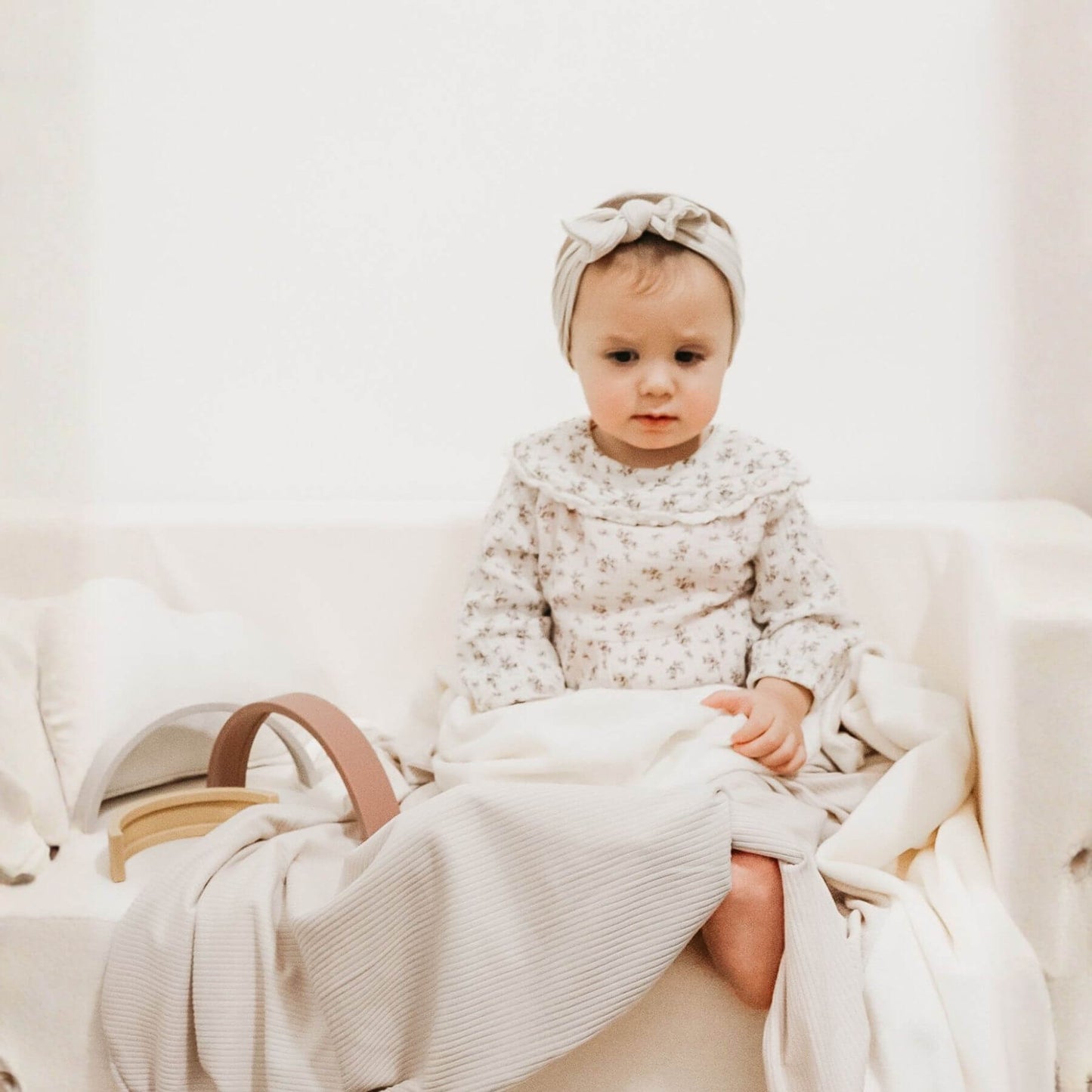 Baby in a floral outfit sitting on Little Mae & Co Oat Ribbed Toddler Blanket