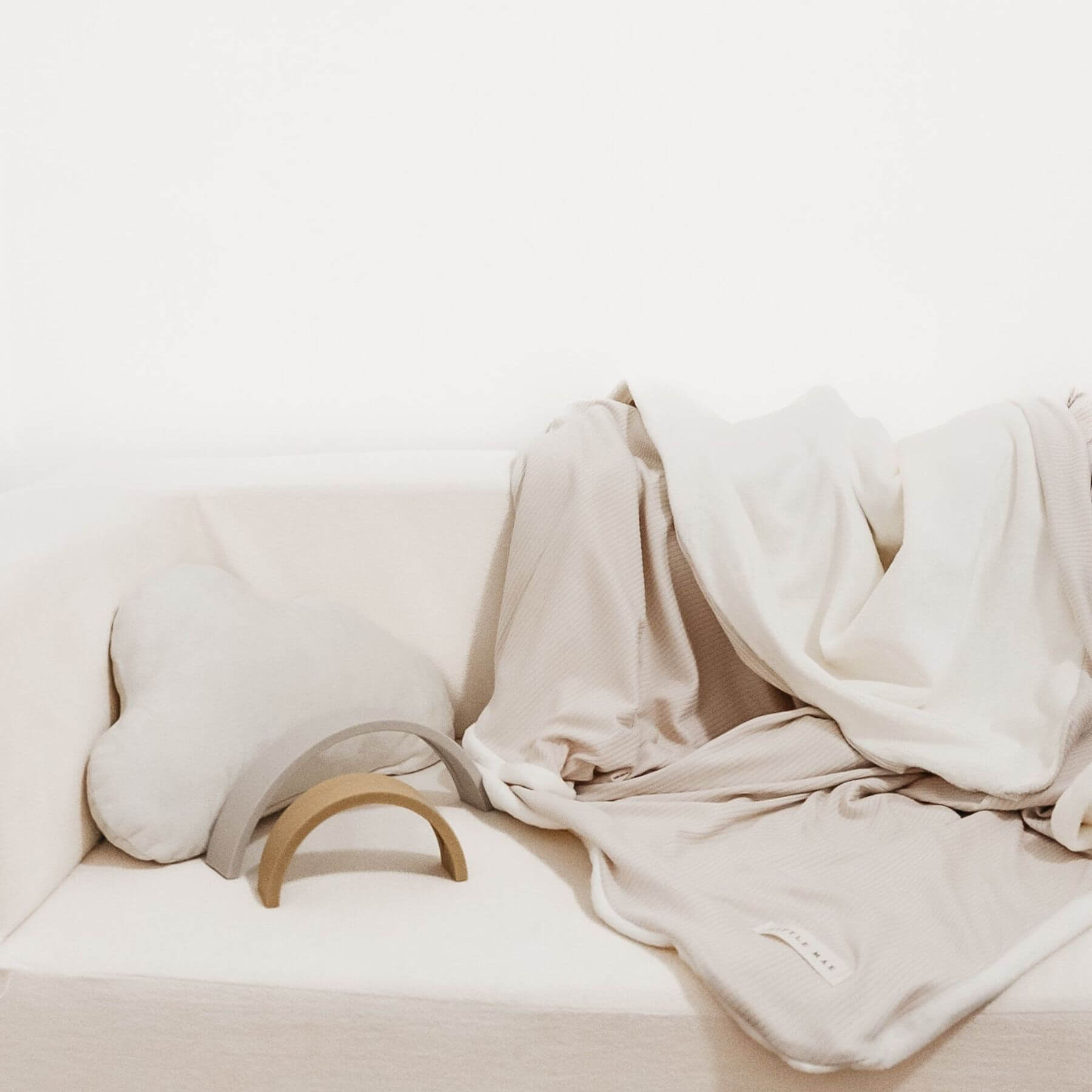 Little Mae & Co Oat Ribbed Toddler Blanket draped over a white sofa with a wooden armrest on a light background