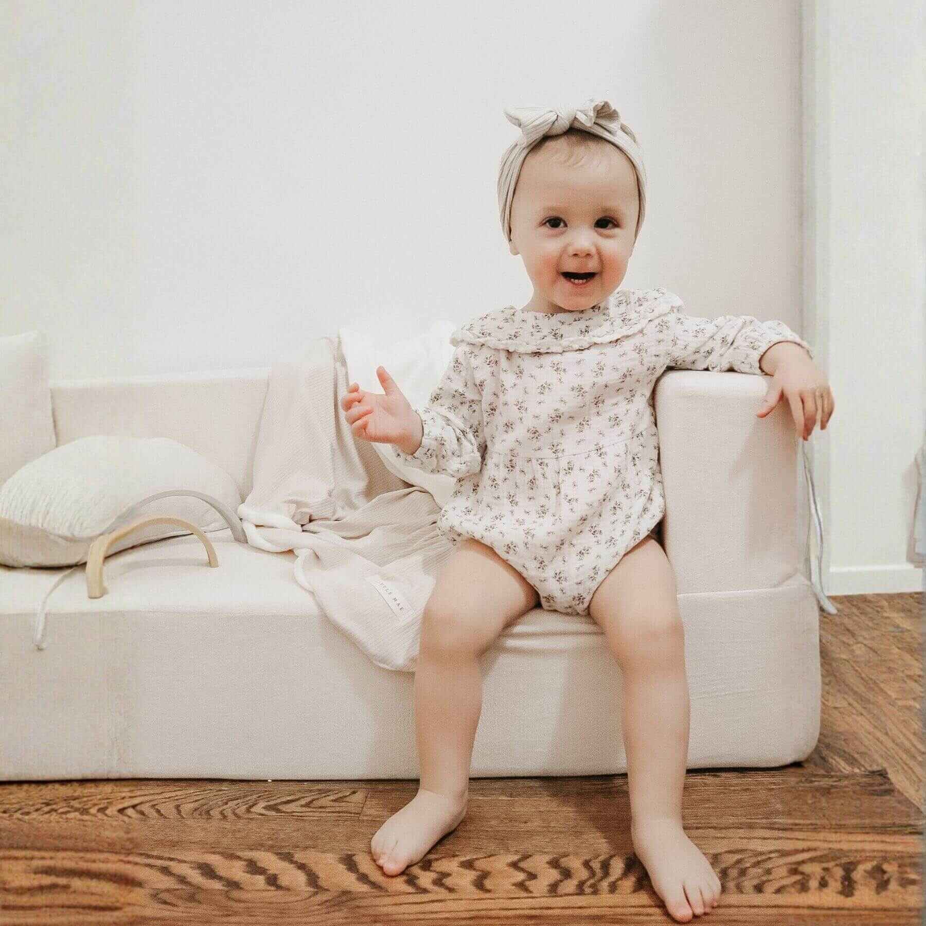 Baby sitting on a couch with Little Mae & Co Oat Ribbed Toddler Blanket in a home setting