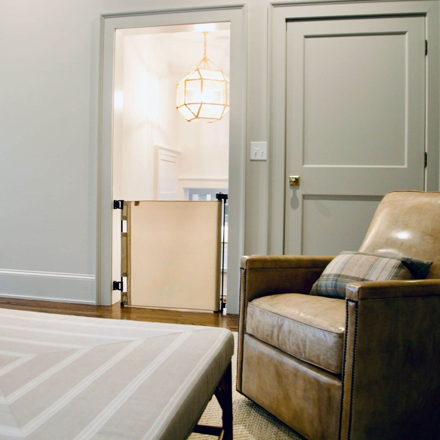 Brown armchair with plaid pillow in a room with a bed and door.