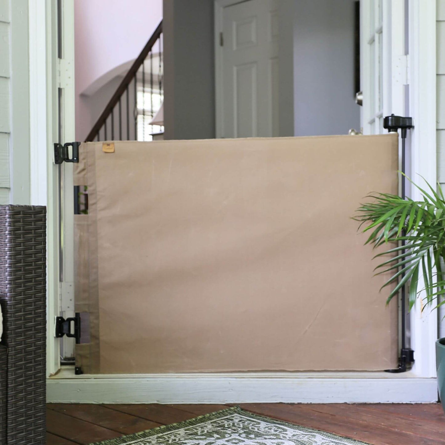 Crafted Gates Co. Oil Waxed Canvas Pet Safety Gate - Tan in a doorway with a plant and rug in the foreground