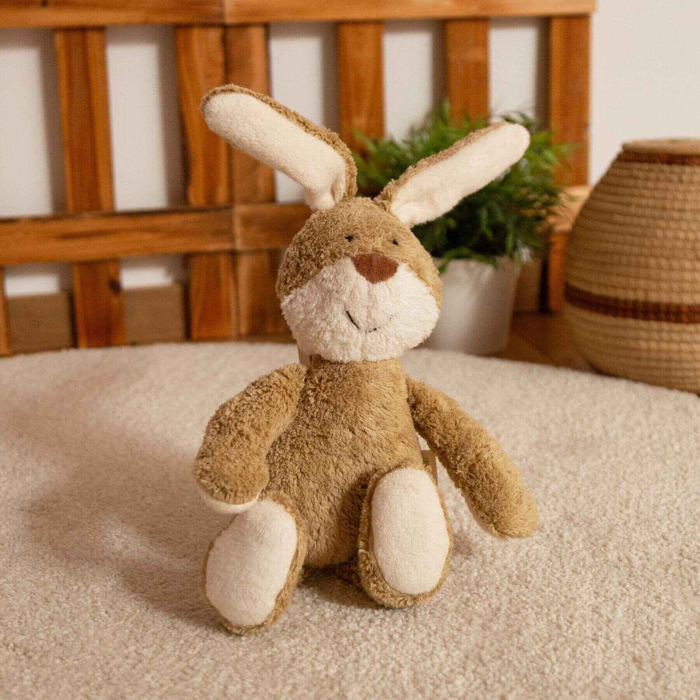 sigikid Organic Bunny Plush Toy on a carpeted floor with a wooden decor and plant in the background