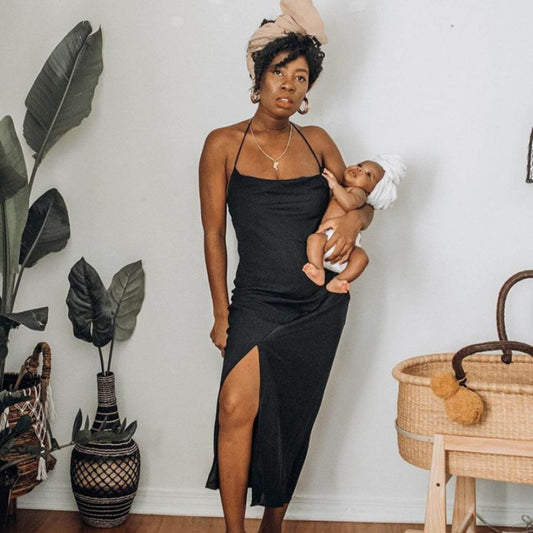 Woman in a black dress holding a baby in a home setting with plants and Plum+Sparrow Original Rocking Moses Bassinet Stand with brake Natural.