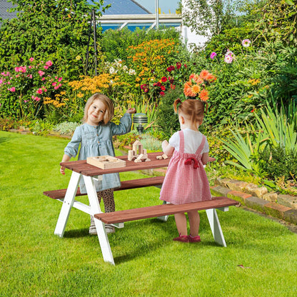 Two children playing at a wooden picnic table in a garden with flowers and greenery.