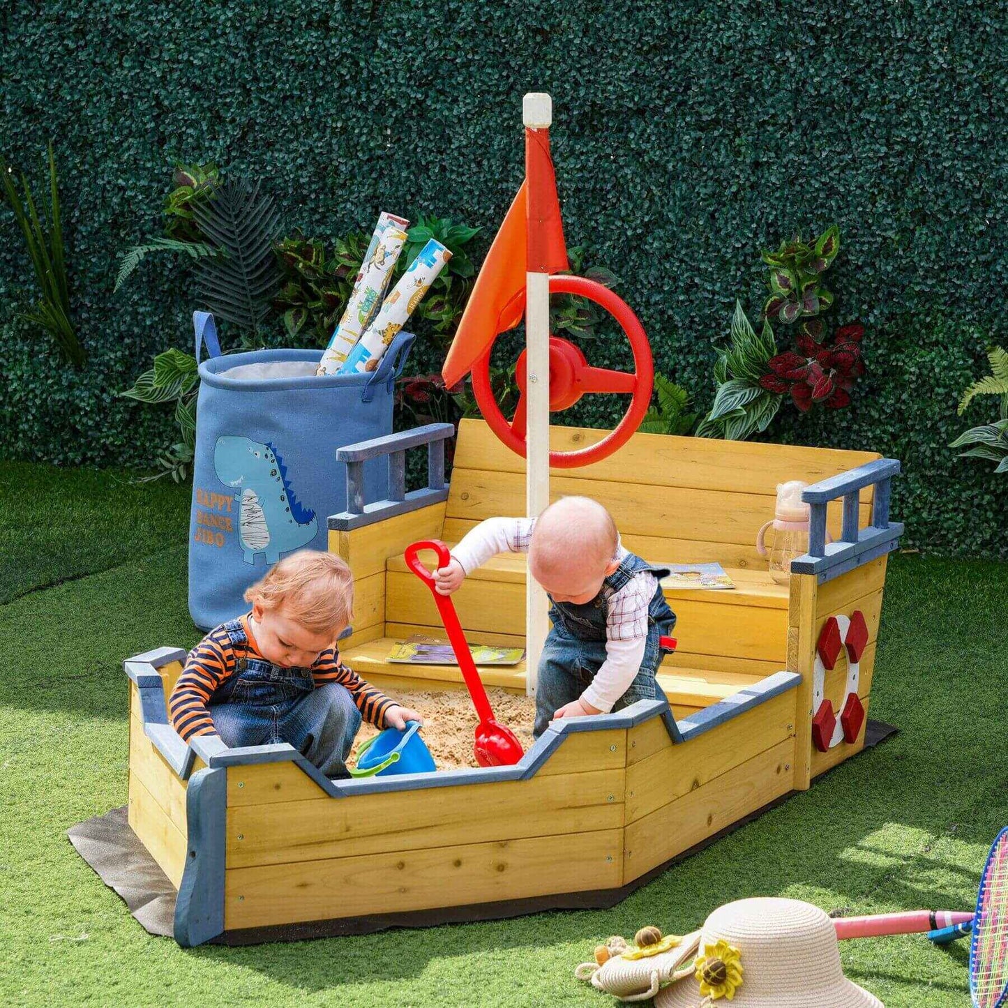 Two children playing in a wooden pirate ship sandbox with toys around.