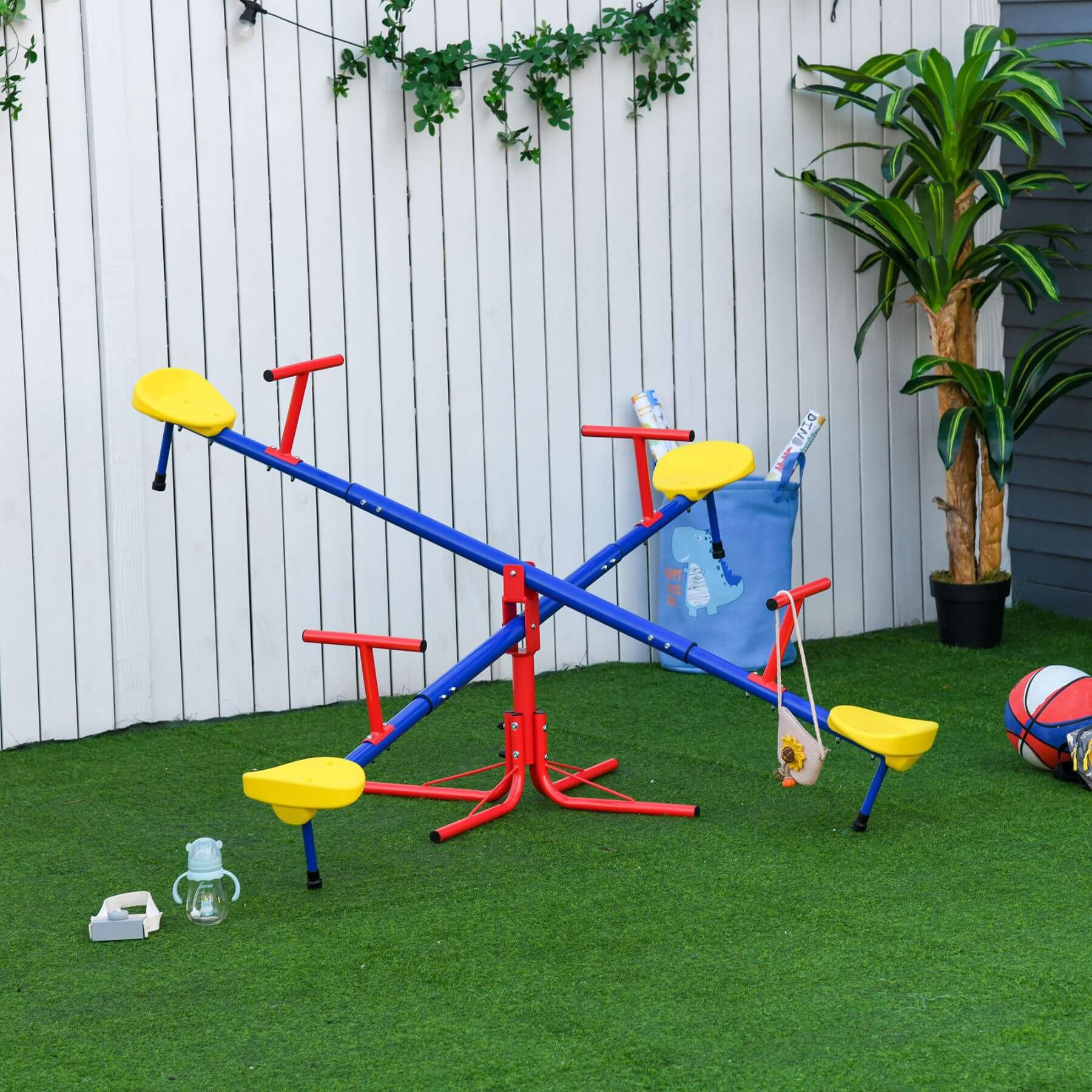 Outsunny Kids 4 Seater Seesaw Swivel Teeter Totter on a grassy area with a white fence and plant in the background