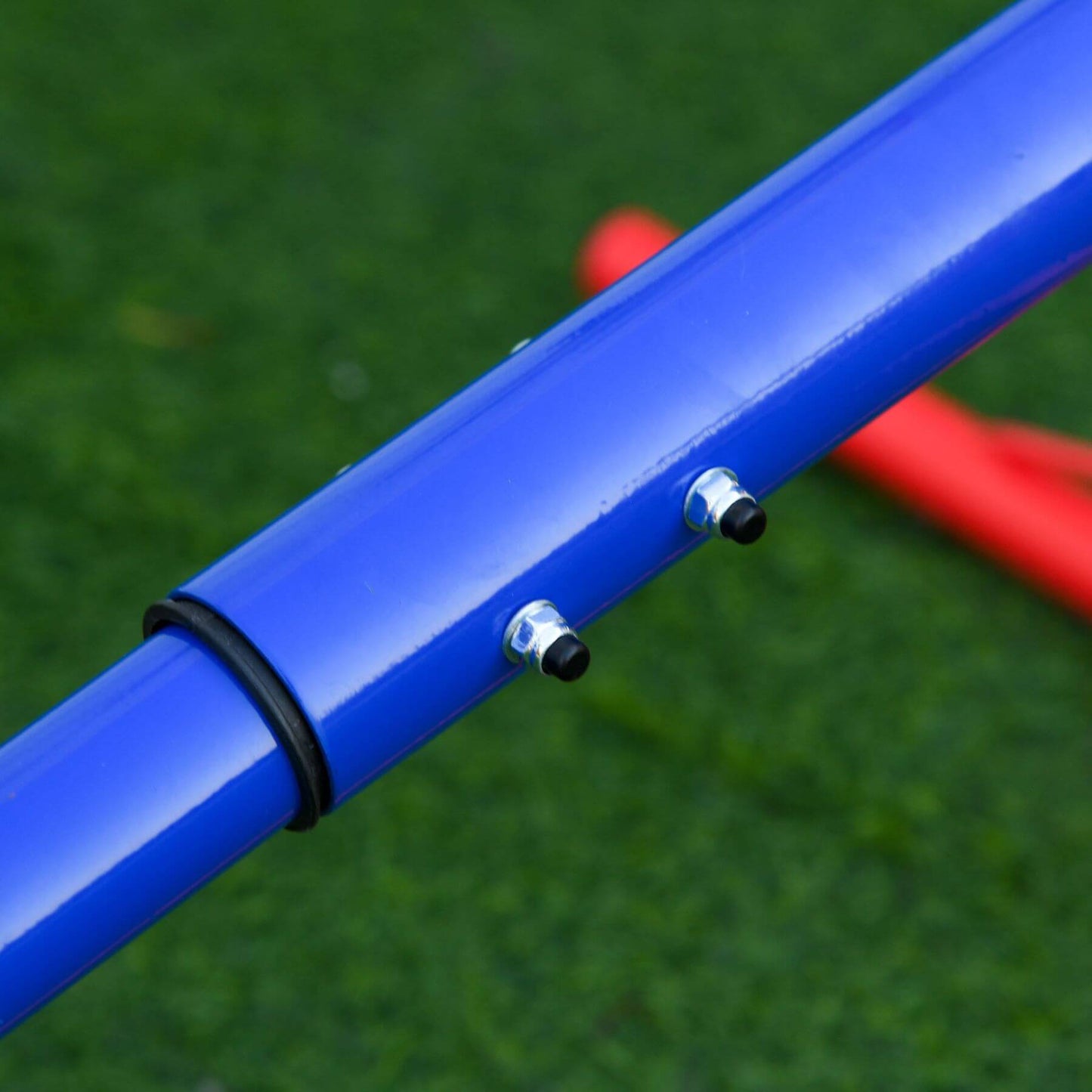 Close-up of a blue metal bar with black rubber band and silver bolts on a green grass background