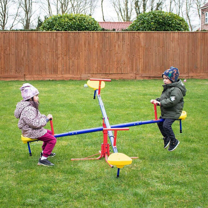 Two children playing on a seesaw in a backyard with a wooden fence and trees in the background.