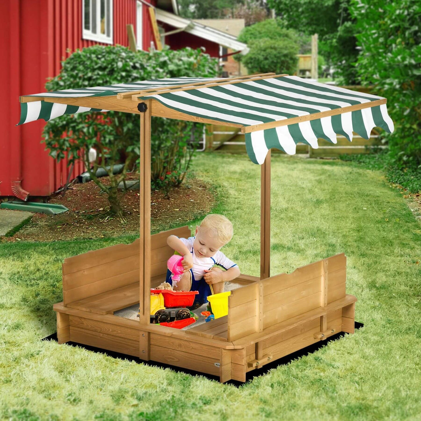 Child playing in a wooden sandbox with a striped canopy in a garden setting.