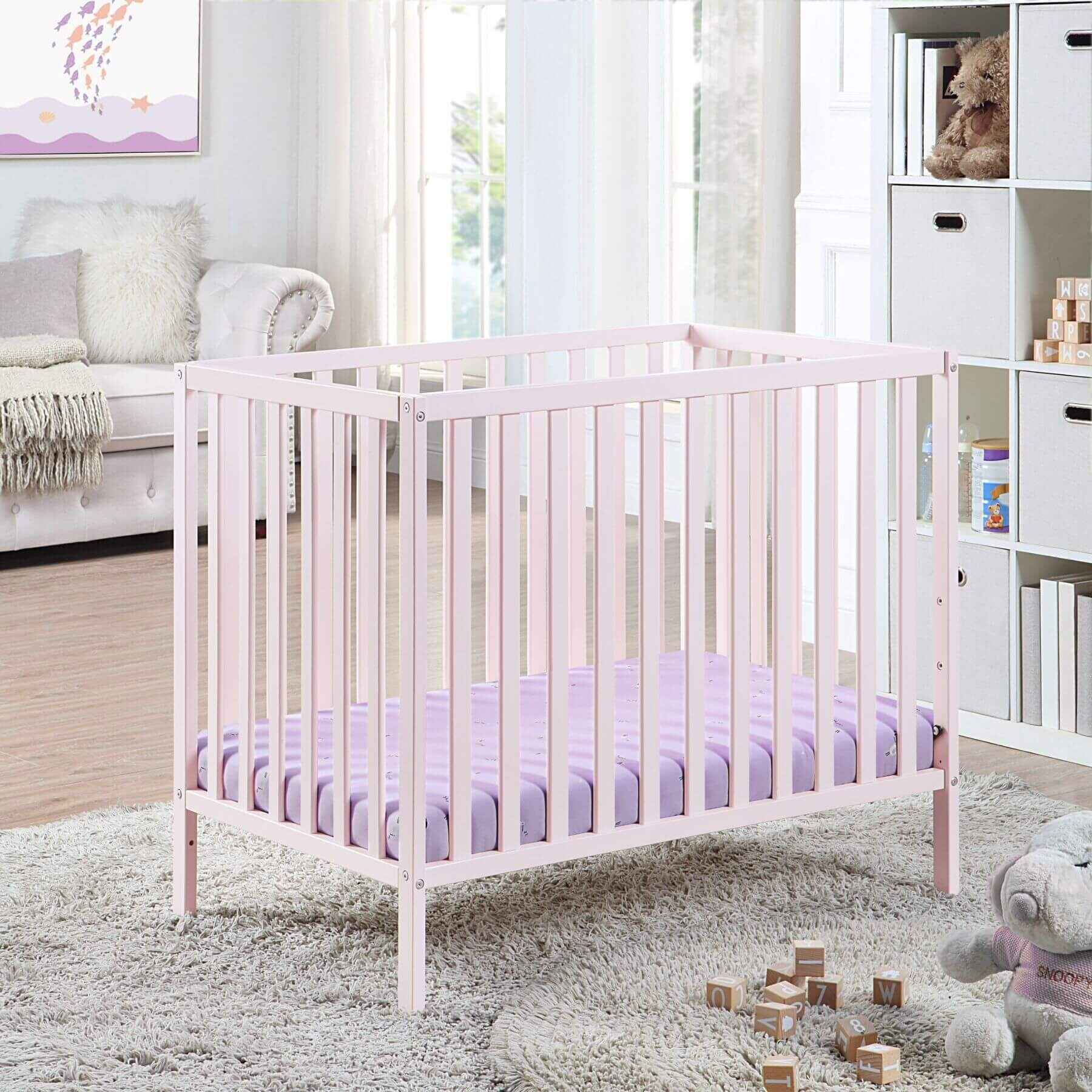 Pink crib with purple mattress in a bright nursery
