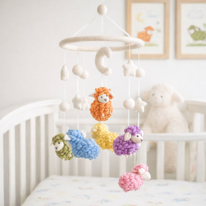 Ganapati Crafts Co. Pastel Sheep Baby Mobile hanging above a crib in a nursery with framed pictures on the wall.