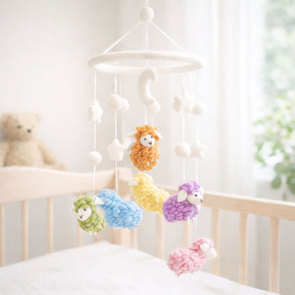 Ganapati Crafts Co. Pastel Sheep Baby Mobile hanging above a crib with a teddy bear in the background.
