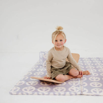 Child sitting on Toki Kids Peace Sign Organic Cotton Mat, wearing a beige sweater and green skirt.