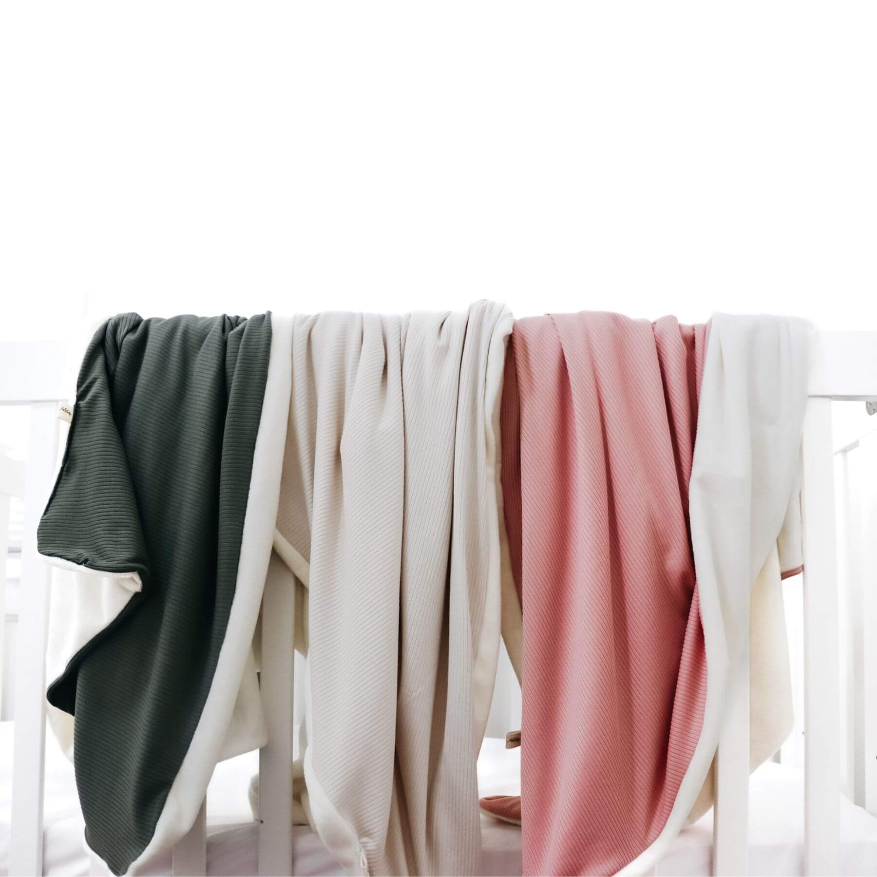 Four different colored blankets draped over a white rack against a white background