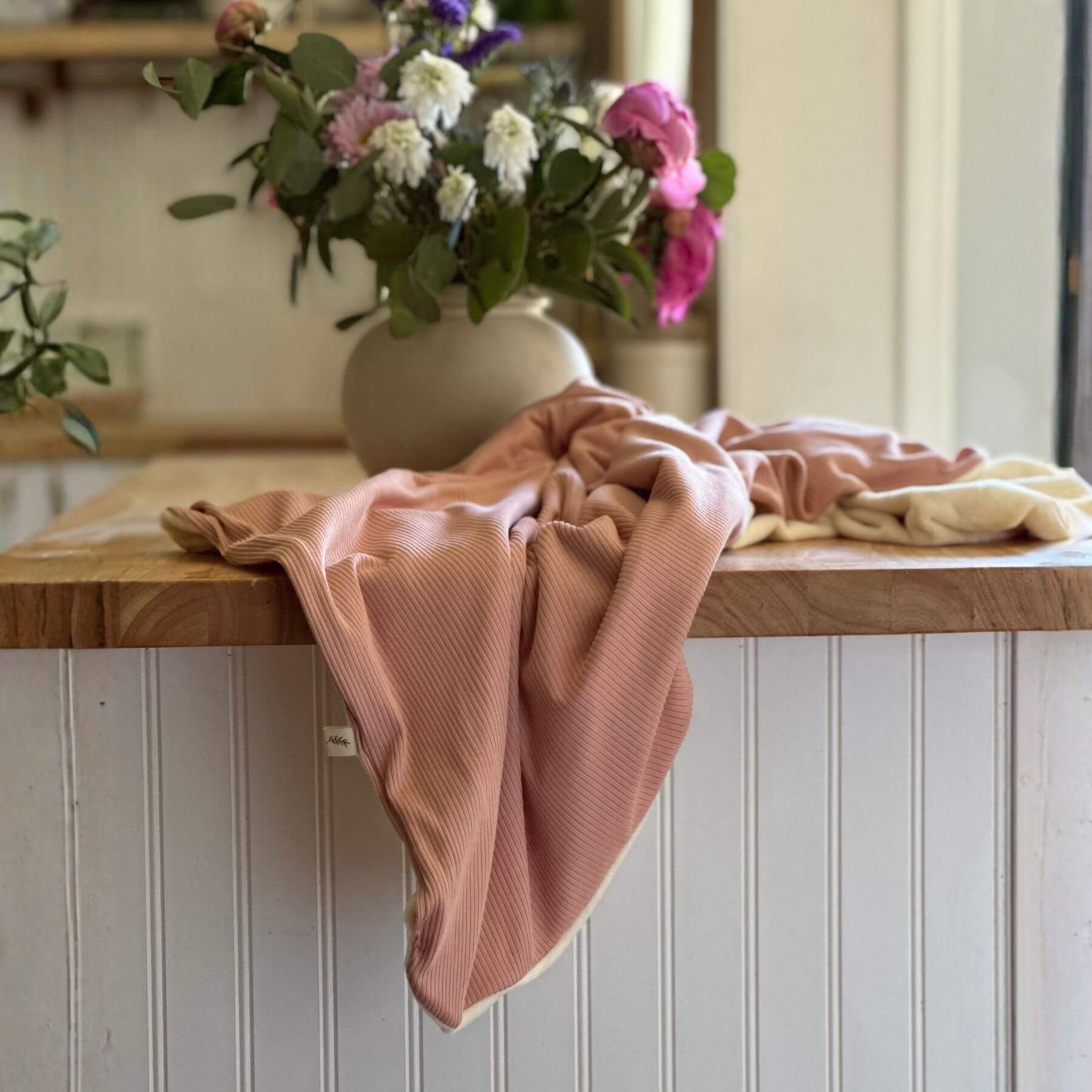 Little Mae & Co Peony Ribbed Toddler Blanket draped over a wooden surface with a vase of flowers in the background
