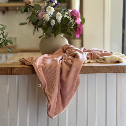 Little Mae & Co Peony Ribbed Toddler Blanket draped over a wooden surface with a vase of flowers in the background