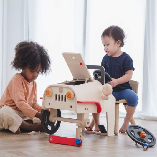 Two children playing with PlanToys Motor Mechanic on a wooden floor.