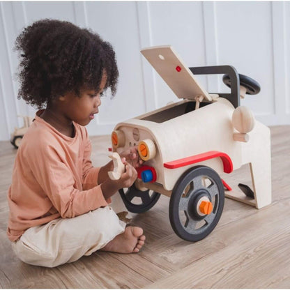 Child playing with PlanToys Motor Mechanic on a wooden floor.