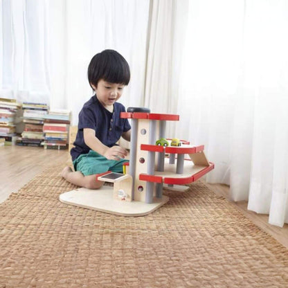 Child playing with PlanToys Parking Garage in a room with books and curtains.