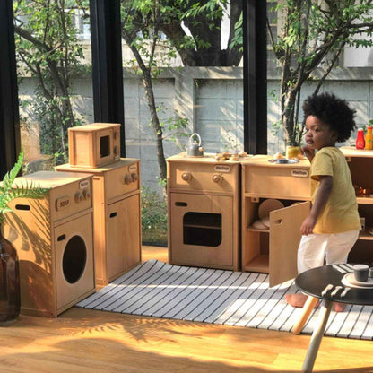 Child playing with a wooden play kitchen set outdoors.
