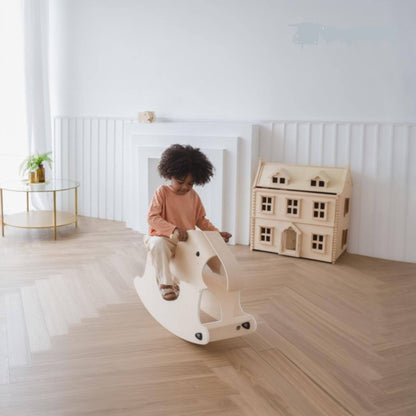 Child playing on PlanToys Walking Elephant in a room with a wooden dollhouse.