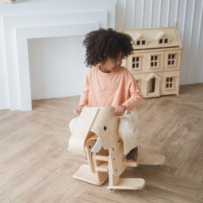 Child playing with PlanToys Walking Elephant in a room with a dollhouse.