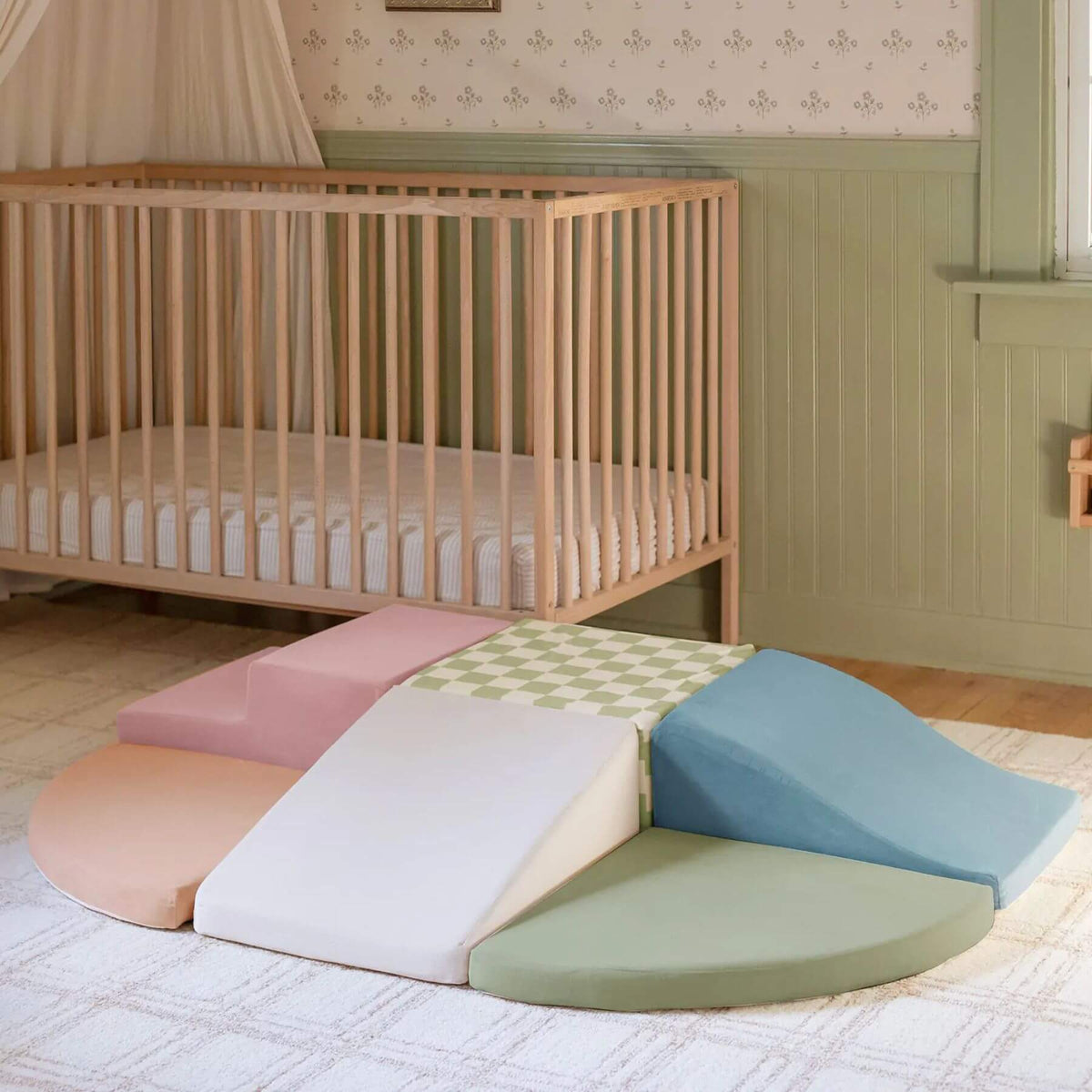 Tiny Land® PlayNest Climbing Blocks - Morandi arranged on a rug in front of a wooden crib in a nursery setting.