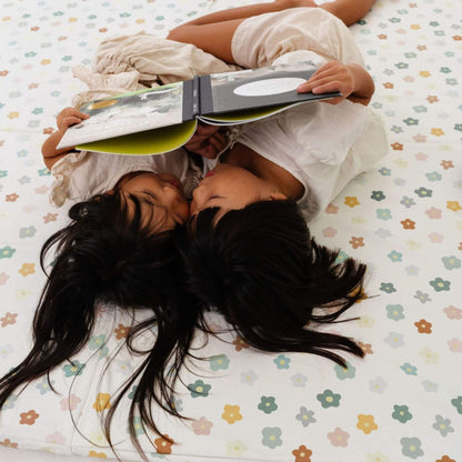 Two people lying on Toki Kids Playful Posies Vegan Leather Mat, one of them reading a book.