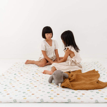 Two young girls sitting on Toki Kids Playful Posies Vegan Leather Mat, one holding a stuffed elephant toy.