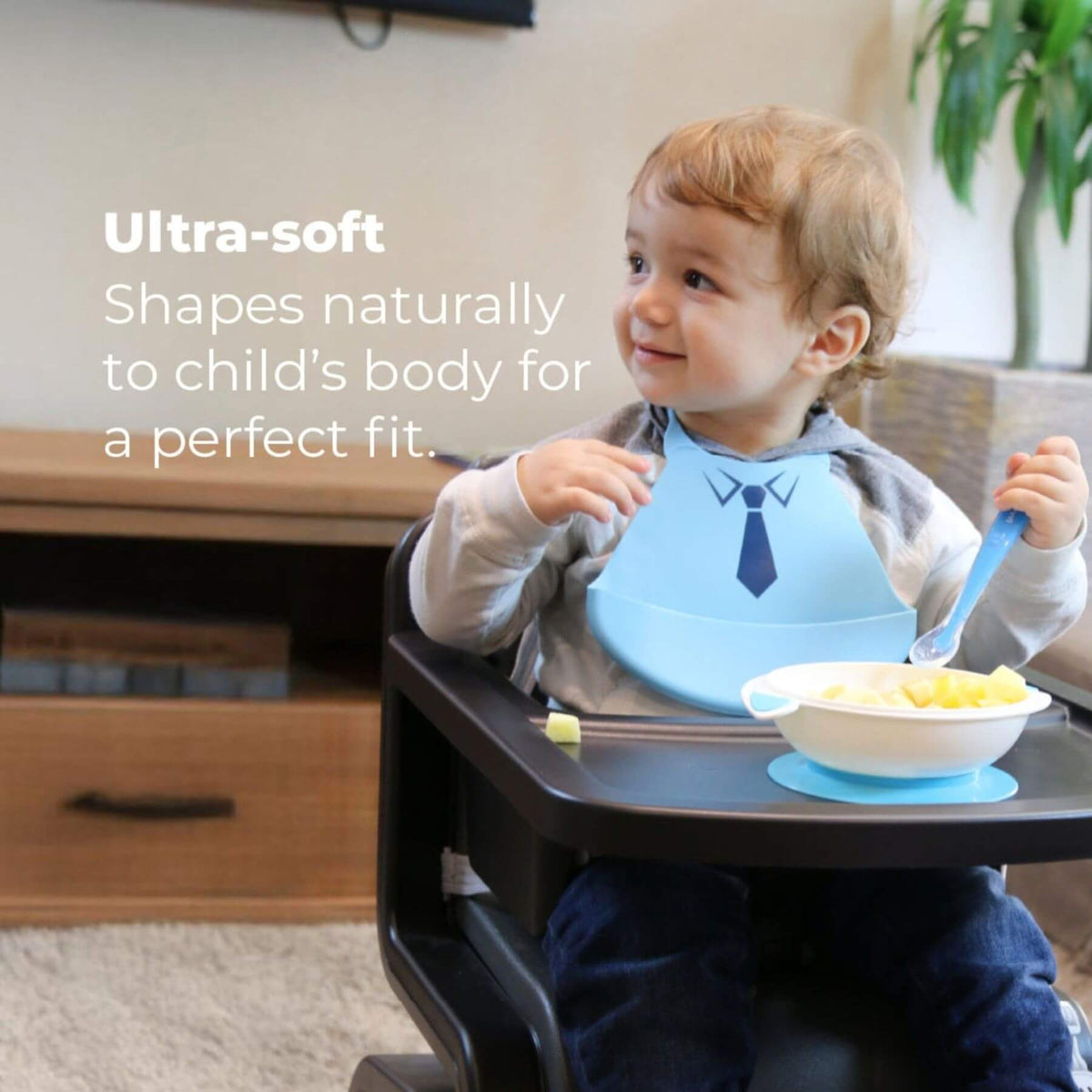 Child sitting in a high chair with a blue bib and bowl, eating.
