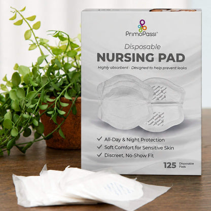 A box of PrimoPassi Disposable Nursing Pads standing on a wooden surface, with a few white pads placed in front and a green potted plant in the background.