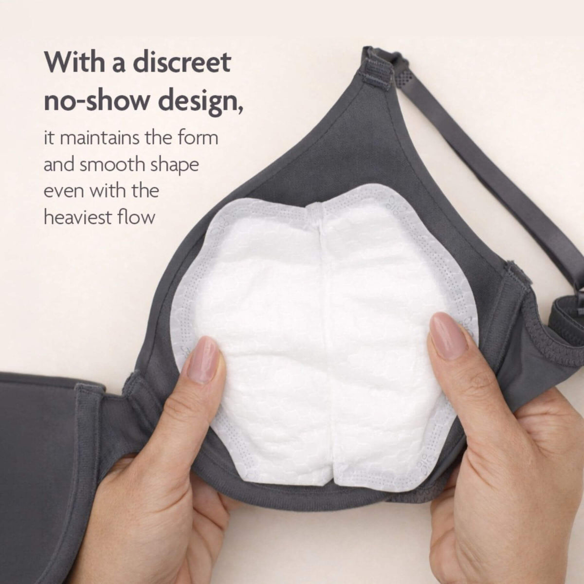 A close-up of a dark gray bra being held open by two hands to show a white, discreet sanitary pad underneath. Text on the left explains the discreet no-show design.