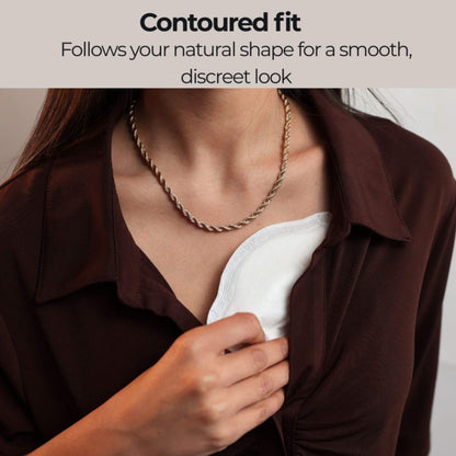 A close-up of a woman wearing a bronze rope chain necklace over a Primo Passi Disposable Nursing Pad and a dark brown collared blouse. Text at the top reads 'Contoured fit Follows your natural shape for a smooth, discreet look'.