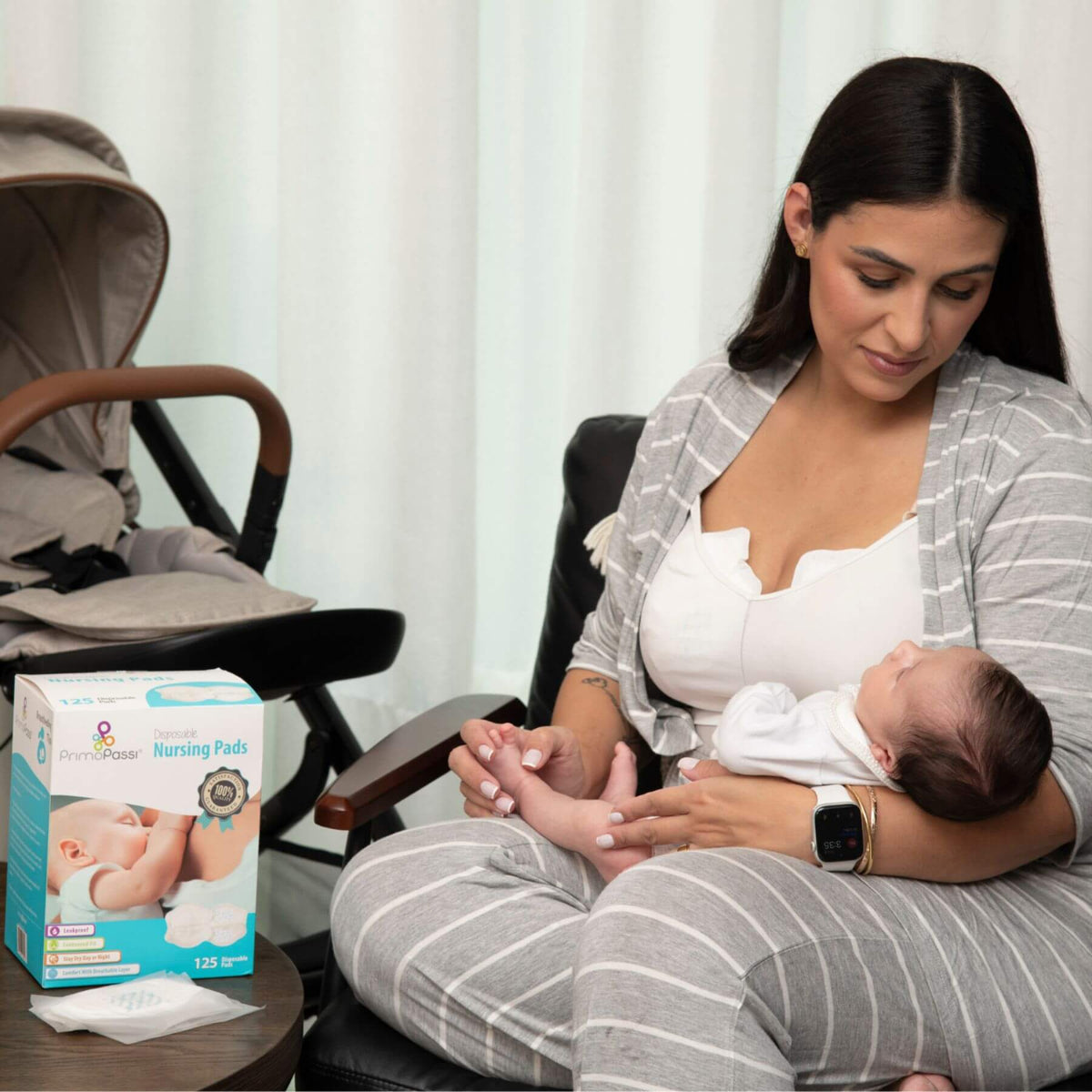 A woman in a gray and white striped nursing outfit holds a baby while sitting in a chair.