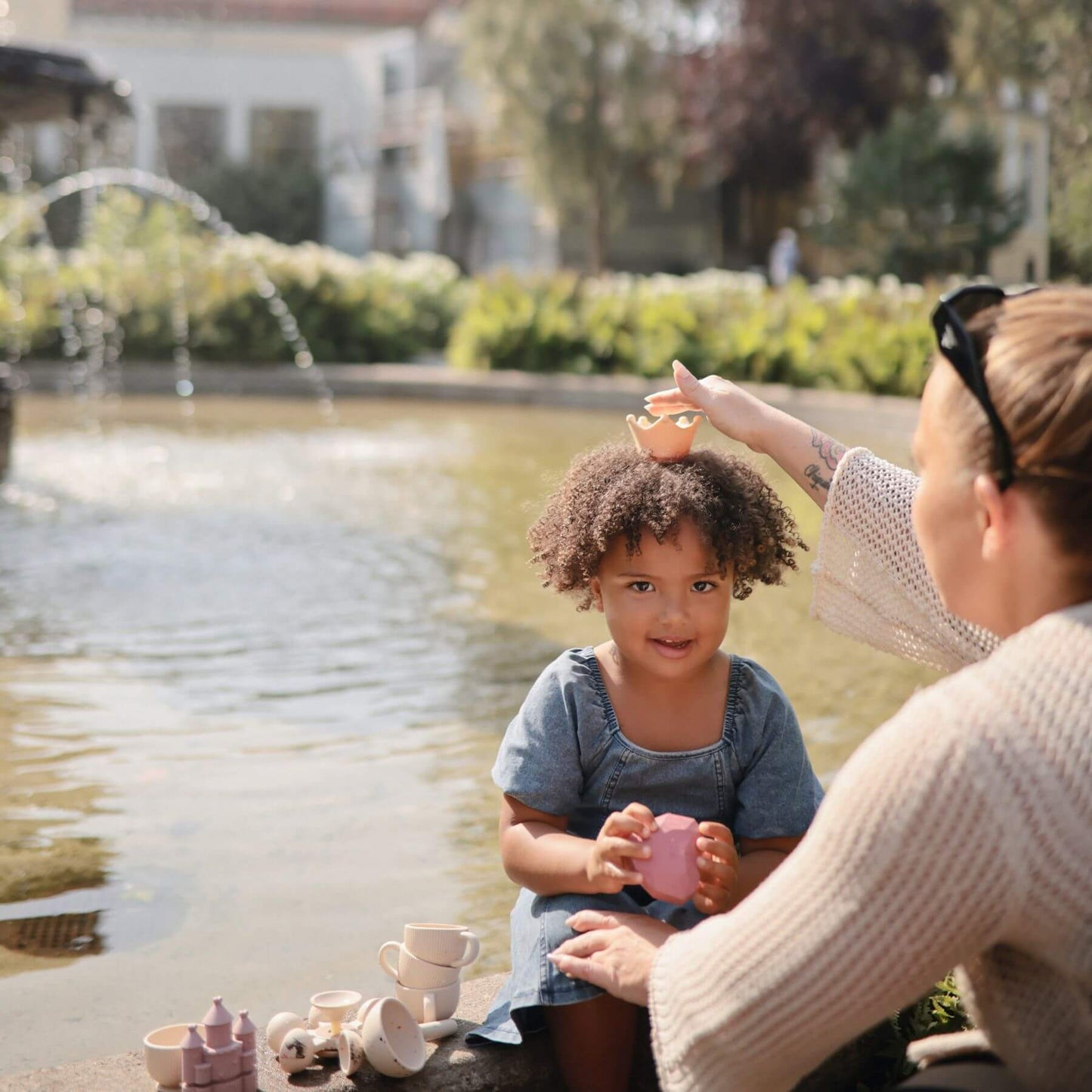 Woman and child playing with Mushie Princess Mold Free Bath Play Set by a fountain in a park