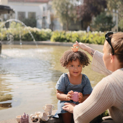 Woman and child playing with Mushie Princess Mold Free Bath Play Set by a fountain in a park