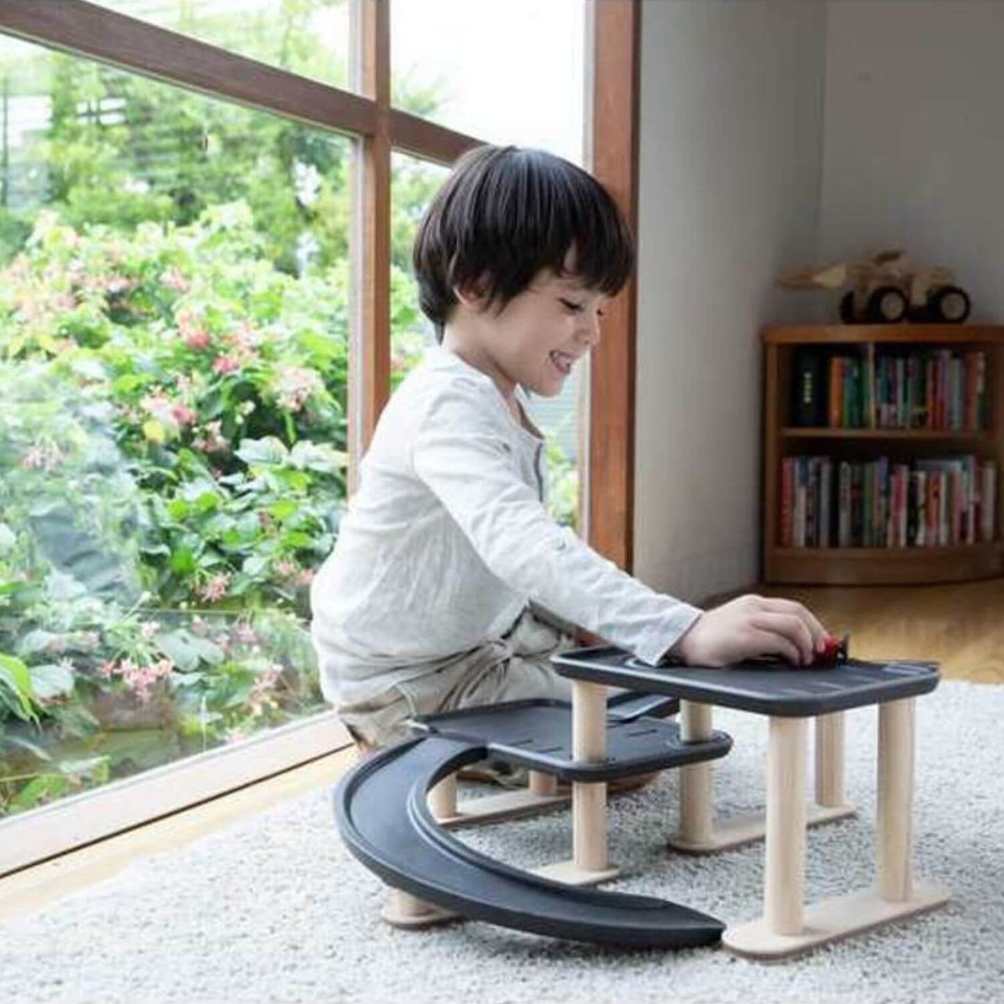 A child sits on floor, playing with PlanToys Race N Play Parking Garage