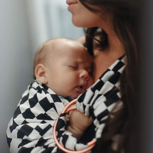 Baby wrapped in Little Mae & Co Race Ring Sling Carrier held by a person.