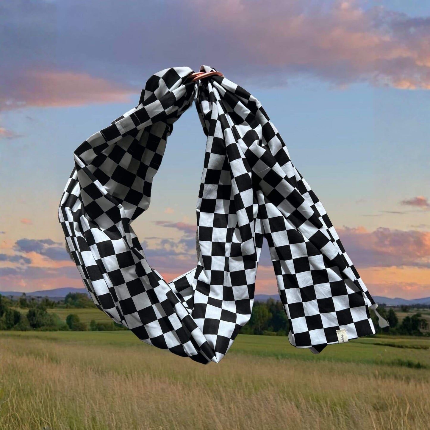 Little Mae & Co Race Ring Sling Carrier held up against a scenic landscape with a sunset.