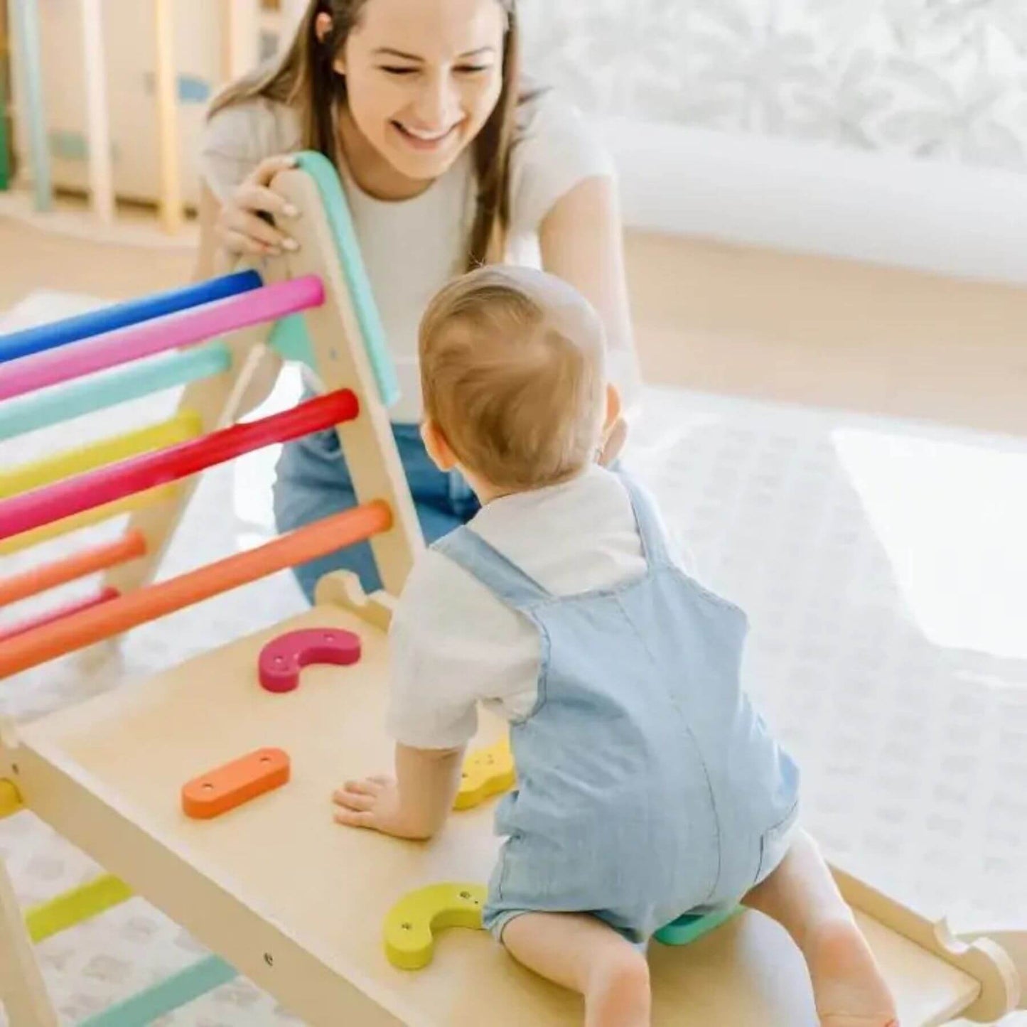 Baby playing with Tiny Land® 7-in-1 Rainbow Pikler Triangle Set with a smiling adult nearby.