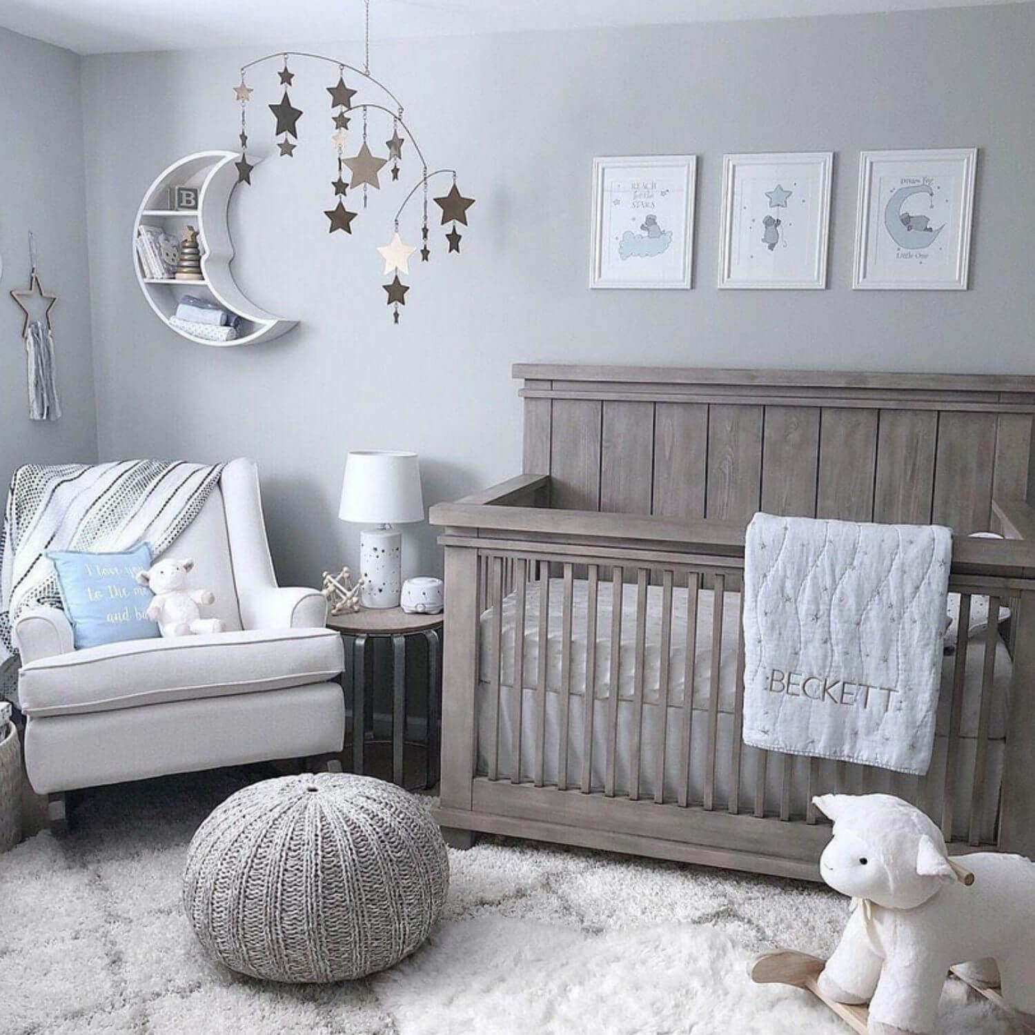 Nursery room with wooden crib, gray chair, and decorative elements on a light gray wall.