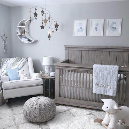 Nursery room with wooden crib, gray chair, and decorative elements on a light gray wall.