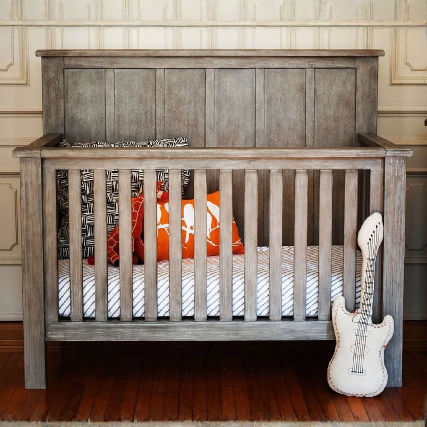 Wooden crib with decorative pillows and a guitar-shaped pillow in a room setting.