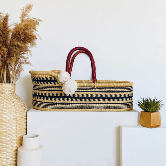 Plum+Sparrow Remy African Moses Basket on a white surface, surrounded by decorative items.