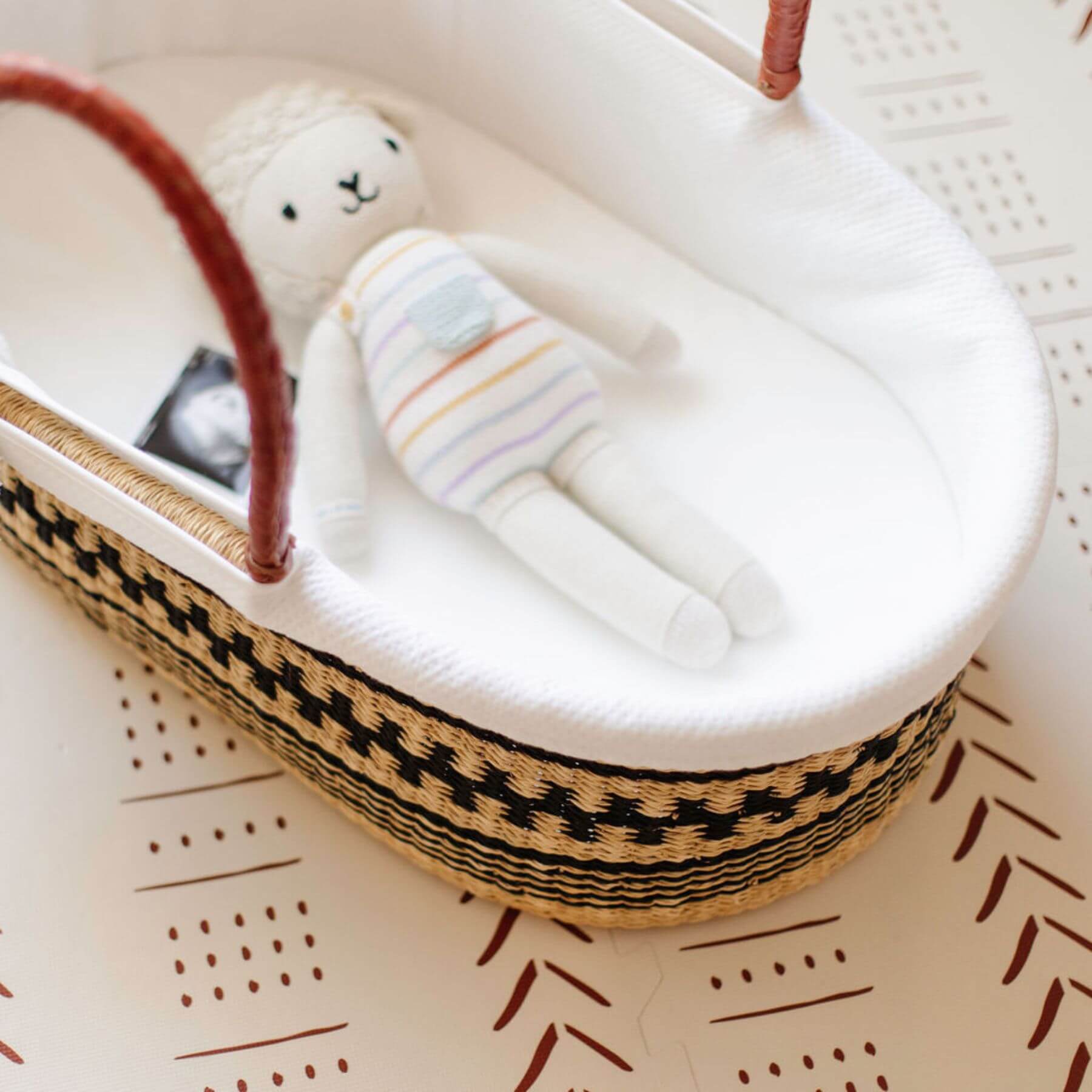 Toy lamb in Plum+Sparrow Remy African Moses Basket on a textured surface