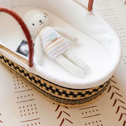 Toy lamb in Plum+Sparrow Remy African Moses Basket on a textured surface