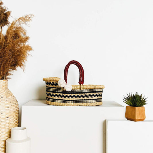 Plum+Sparrow Remy Mini Moses Basket on a white surface with decorative plants.